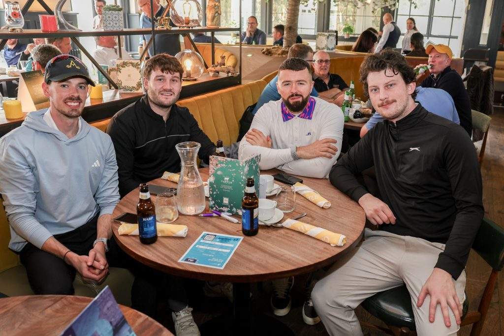 Four men sat at a round table with beers after the golf, smiling at the camera.
