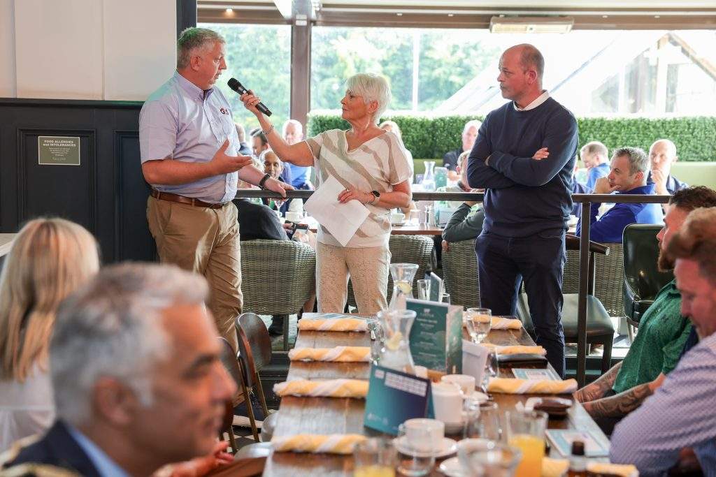 NI Chamber's Annual golf day, shot of three people at the front of the restaurant - Kevin Scruby of G4s speaking into the microphone.