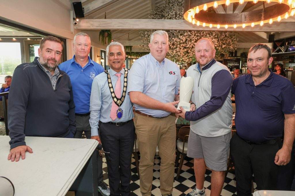 G4S's Kevin Scruby and NI Chamber President, Kailash Chada, standing with four prize winners smiling at the camera, holding a trophy.