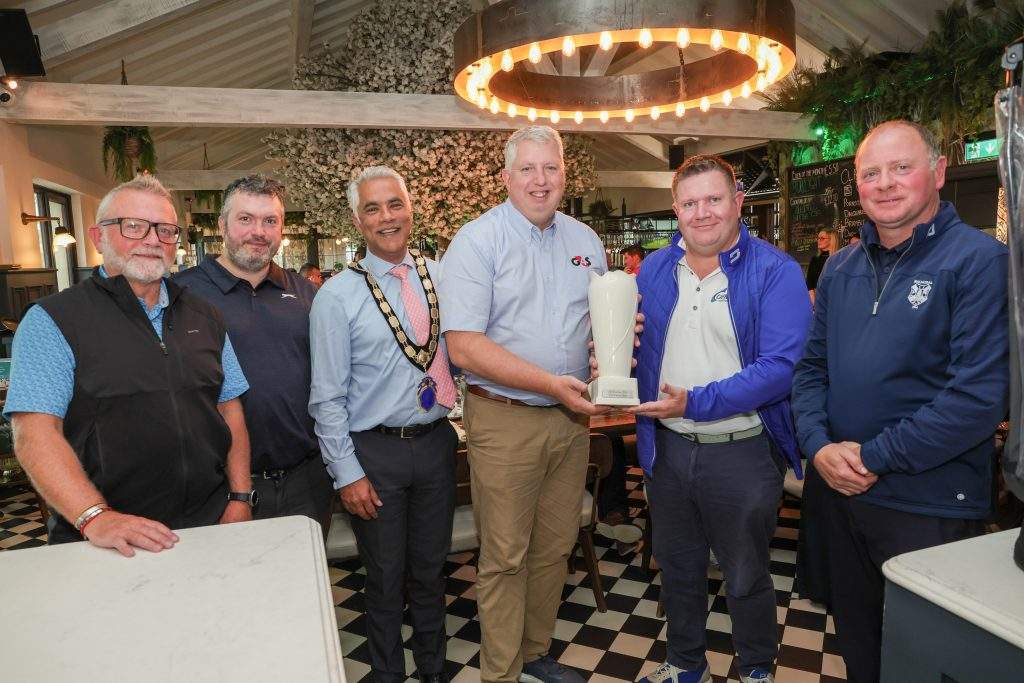 G4S's Kevin Scruby and NI Chamber President, Kailash Chada, standing with four new prize winners smiling at the camera, holding a trophy.