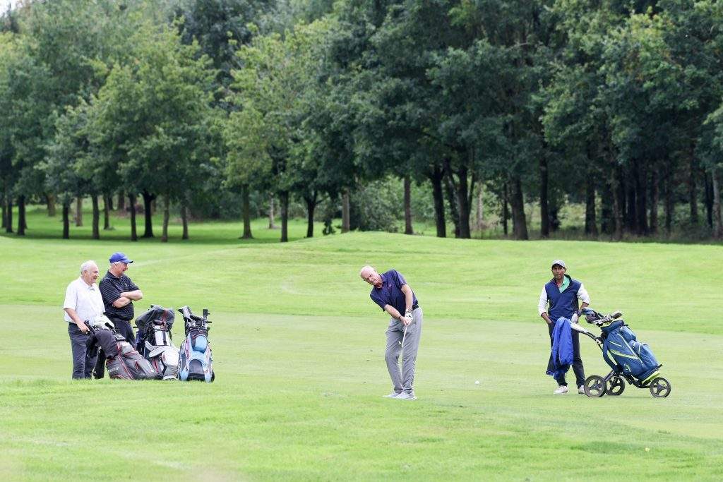 Four golfers on the green. Three watching one golfer take a swing from a different angle 