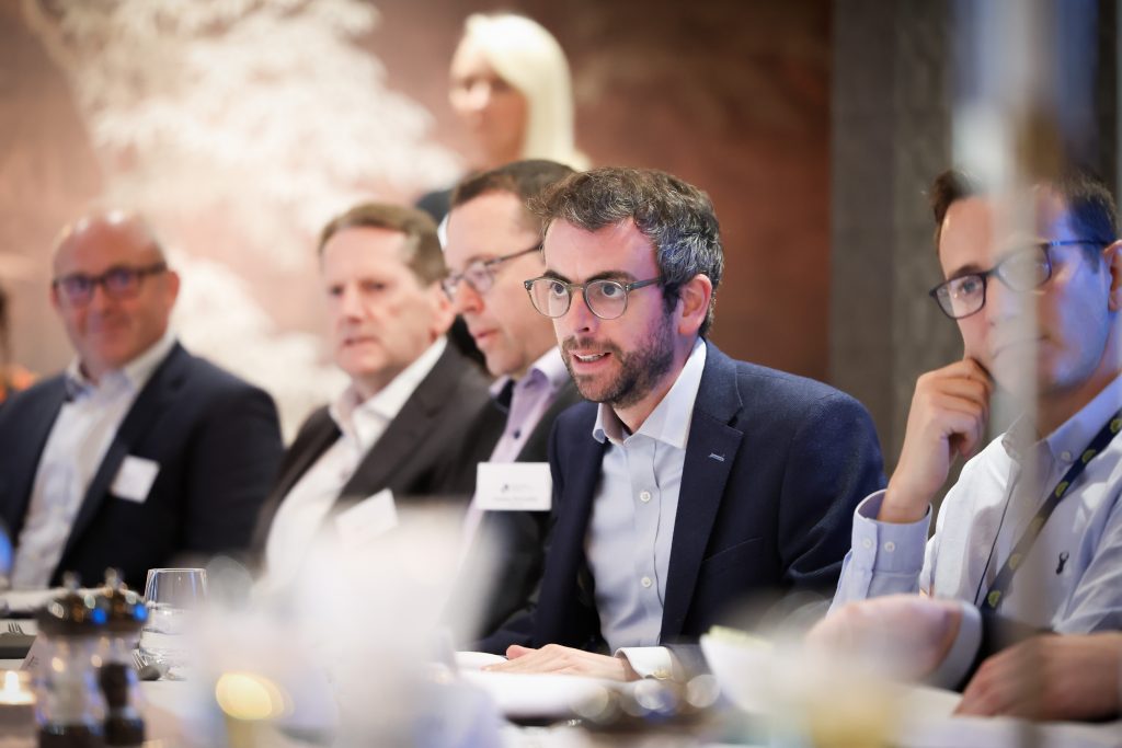 NI Chamber In Camera event with Department for Communities. soft lighting with people at a table - Stuart Anderson, NI Chamber speaking with three people in the background: Petrina McAuley and two others