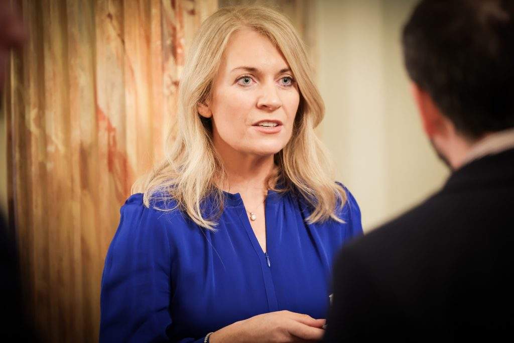 A person wearing a blue outfit engaging in conversation with others in a warmly lit room with decorated walls.