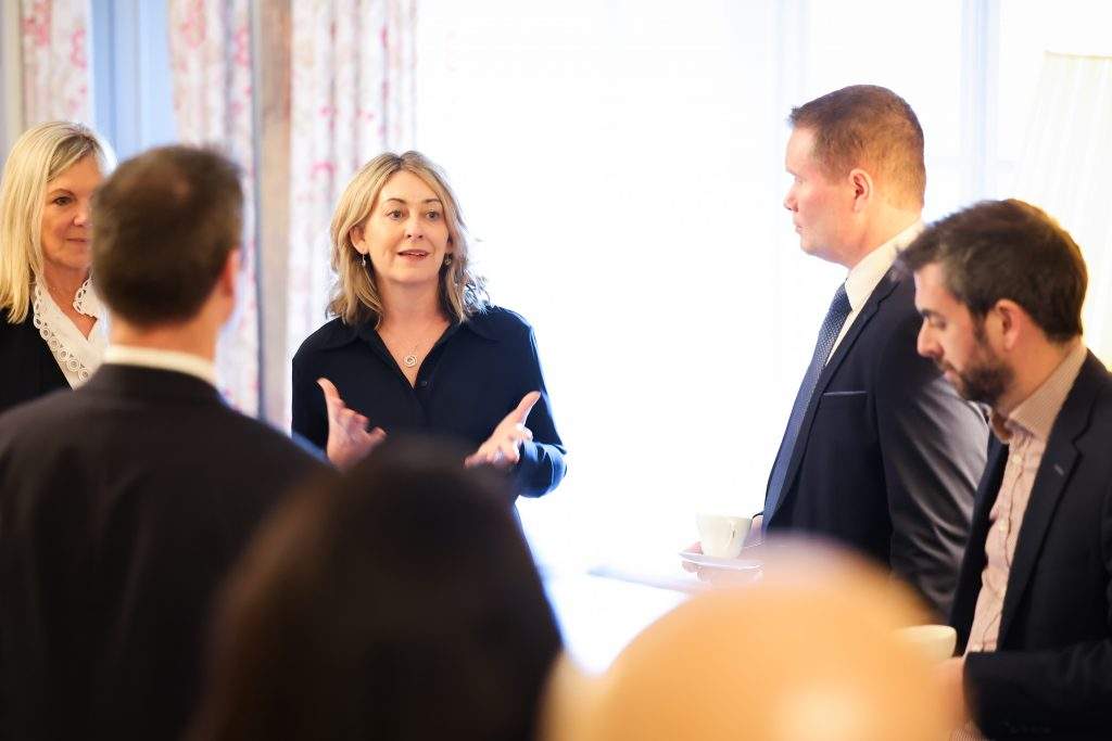 A group of people standing together in a bright room, talking while holding cups during a networking-style gathering.