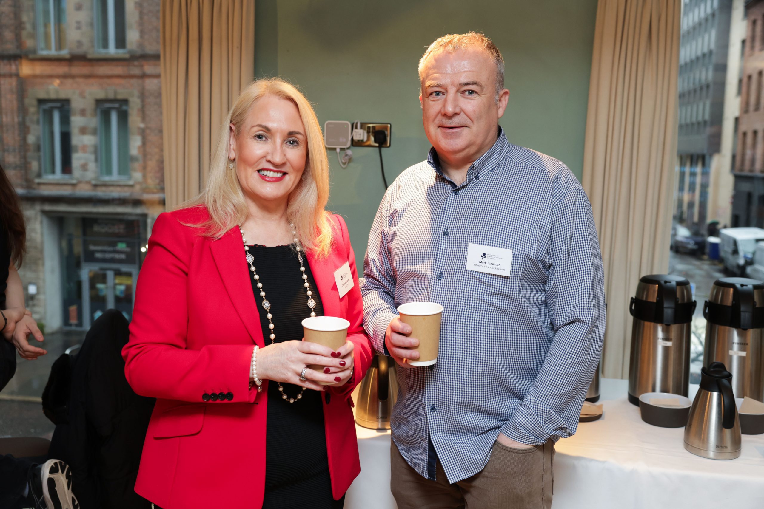 Two attendees standing together near a refreshments area, each holding a coffee cup.