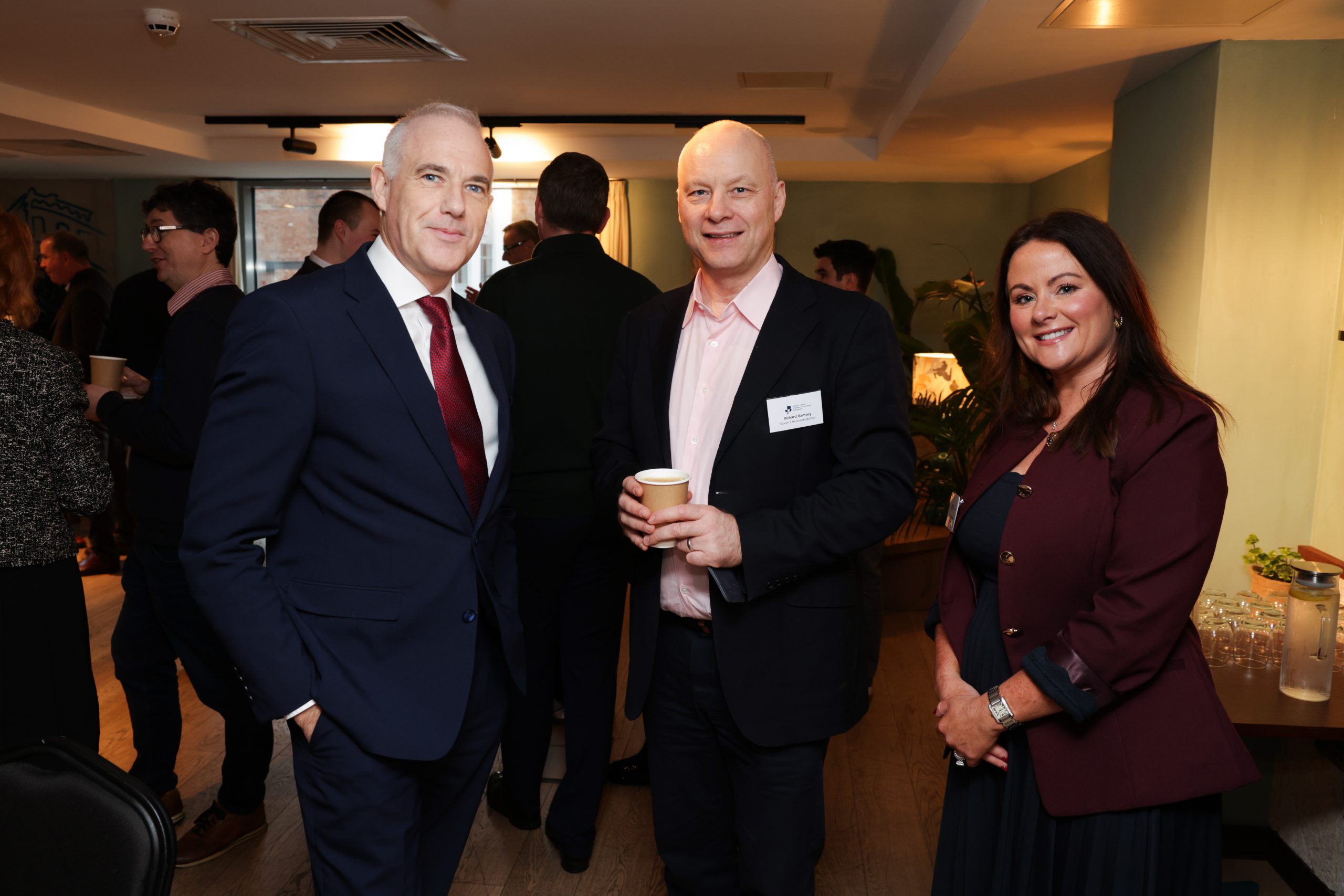 A small group of attendees standing together in a networking area, holding coffee cups and talking.