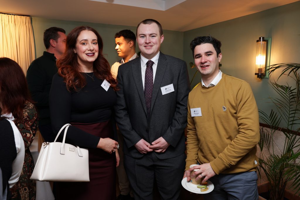 Three attendees posing together at a networking event, one holding a small plate with refreshments.