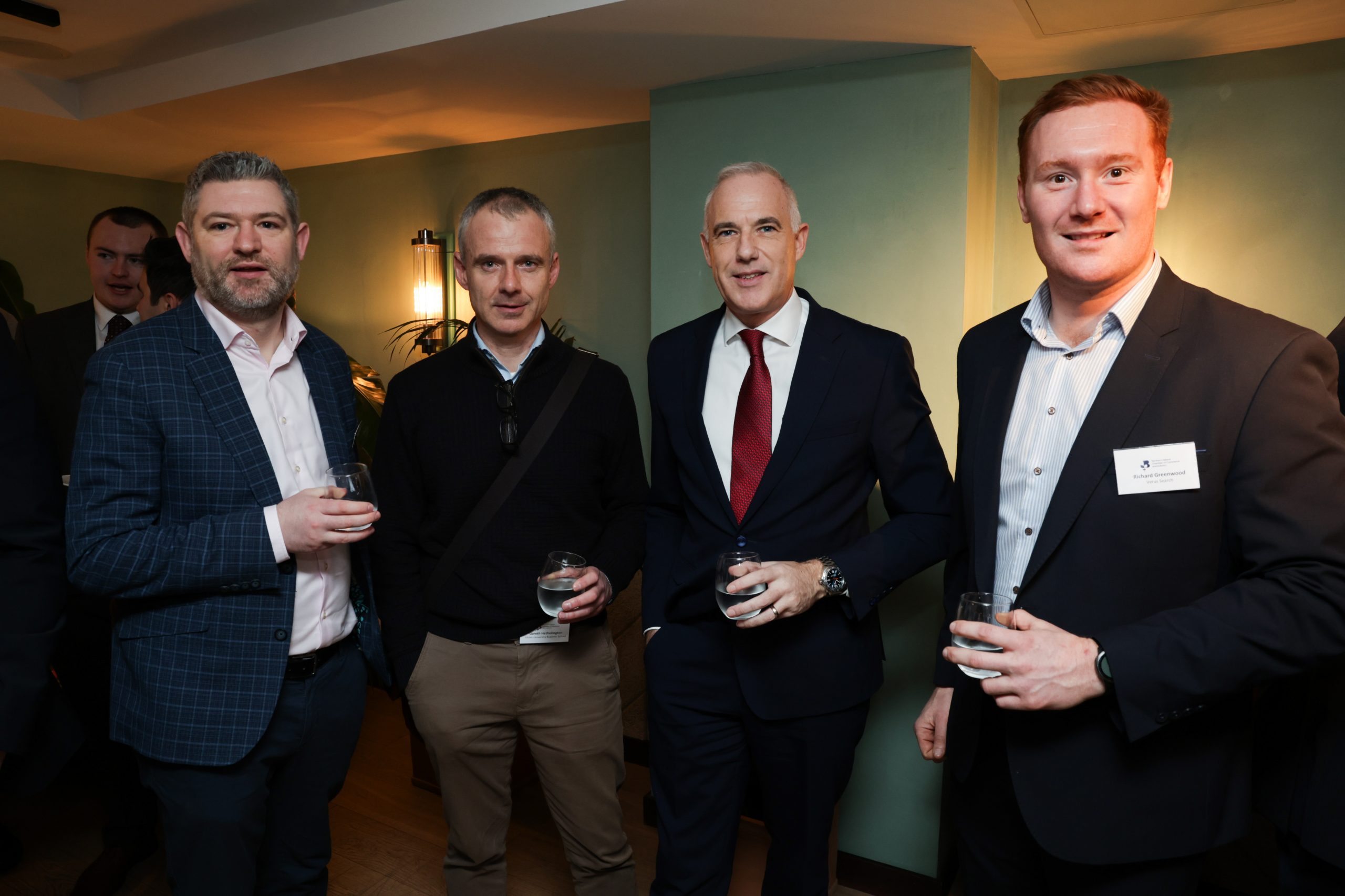 Four people standing in a group at a networking event, each holding a drink while chatting.
