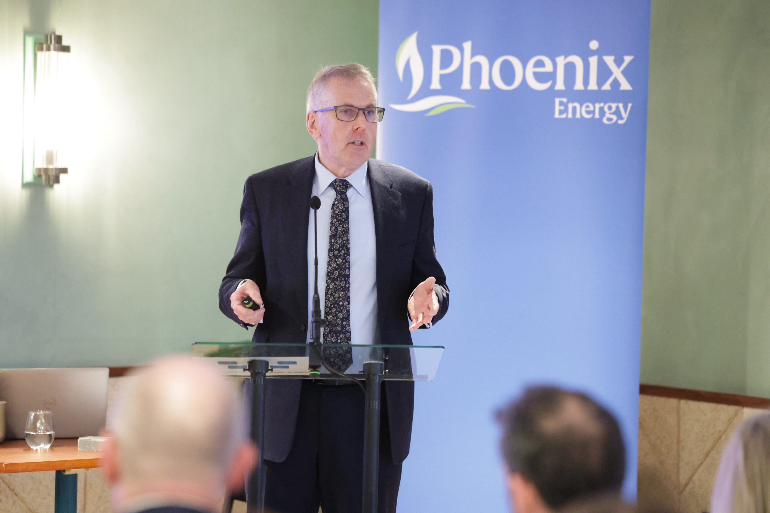 A speaker standing at a lectern delivering a presentation in front of a “Phoenix Energy” backdrop.