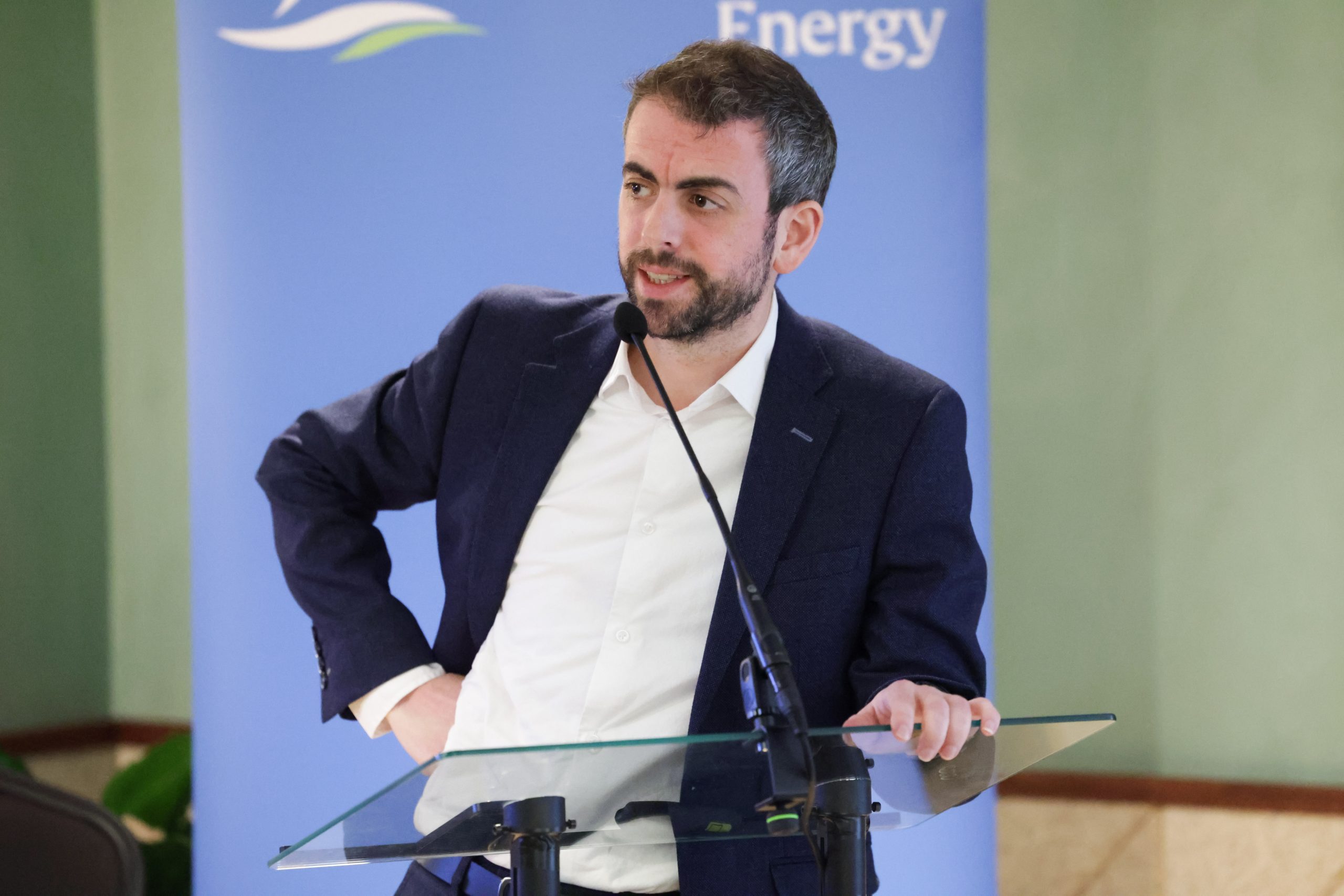 A speaker standing behind a glass lectern in front of a branded “Phoenix Energy” backdrop.