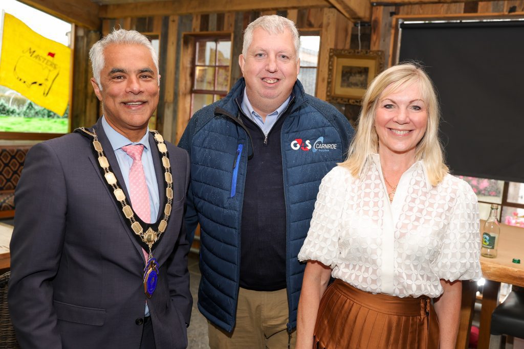 NI chamber ceo, Suzanne Wylie, with ni chamber president, Kailash Chada and the golf day sponsor, Kevin Scruby of G4S, standing in the bar at the Galgorm, called 'The Barn', smiling at the camera