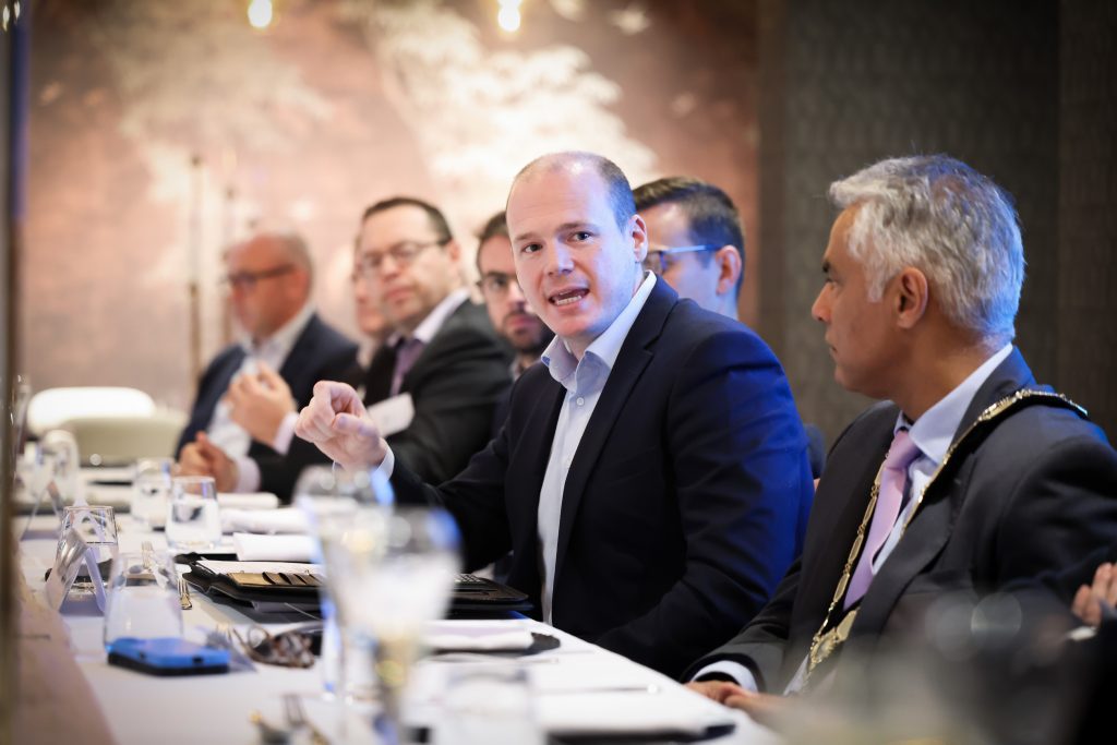  Minister for Communities, Gordon Lyons speaking to Kailash Chada and others on one side of the table, six people in the shot.
