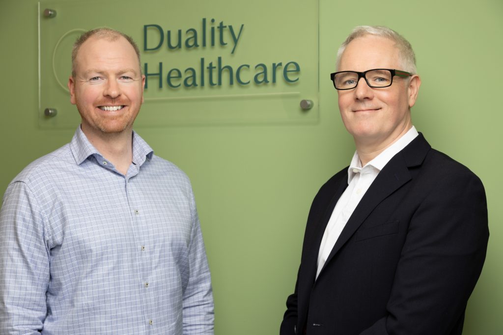Two men standing in front of a Duality Healthcare sign