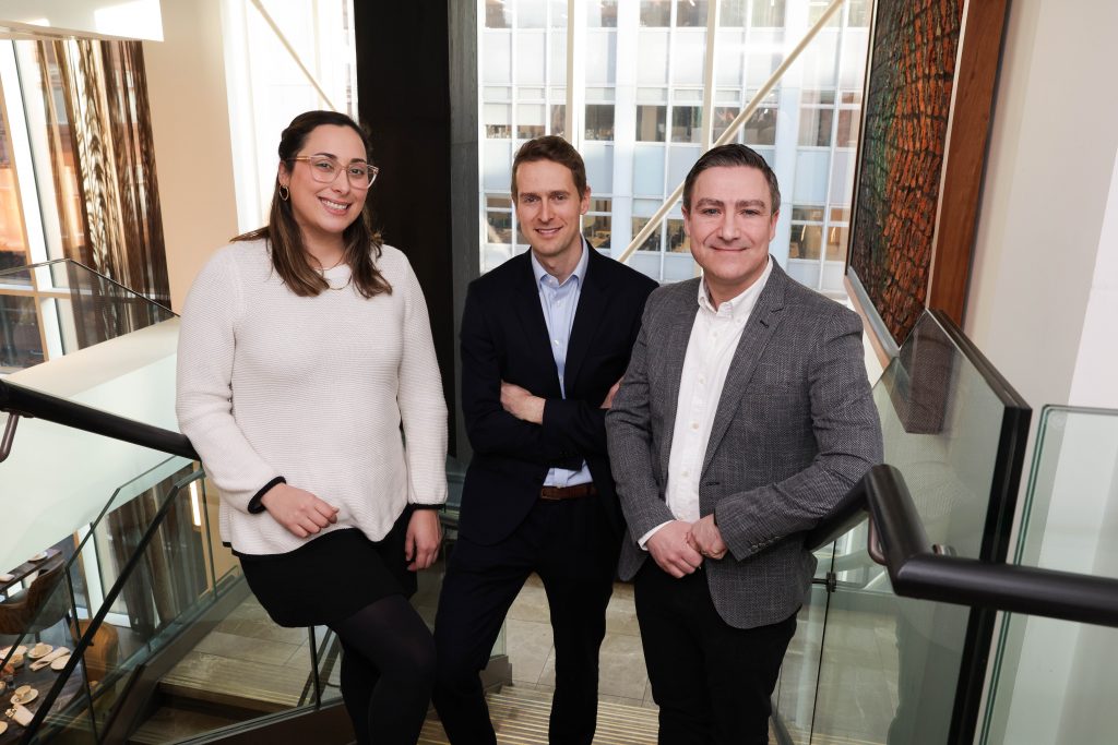 Three people stand together on a staircase in a bright atrium with glass walls and modern architectural features.