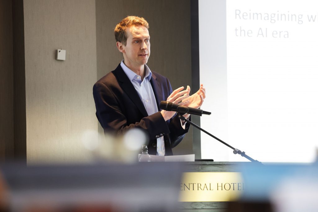a speaker stands at a podium with a microphone, addressing the audience during a presentation.