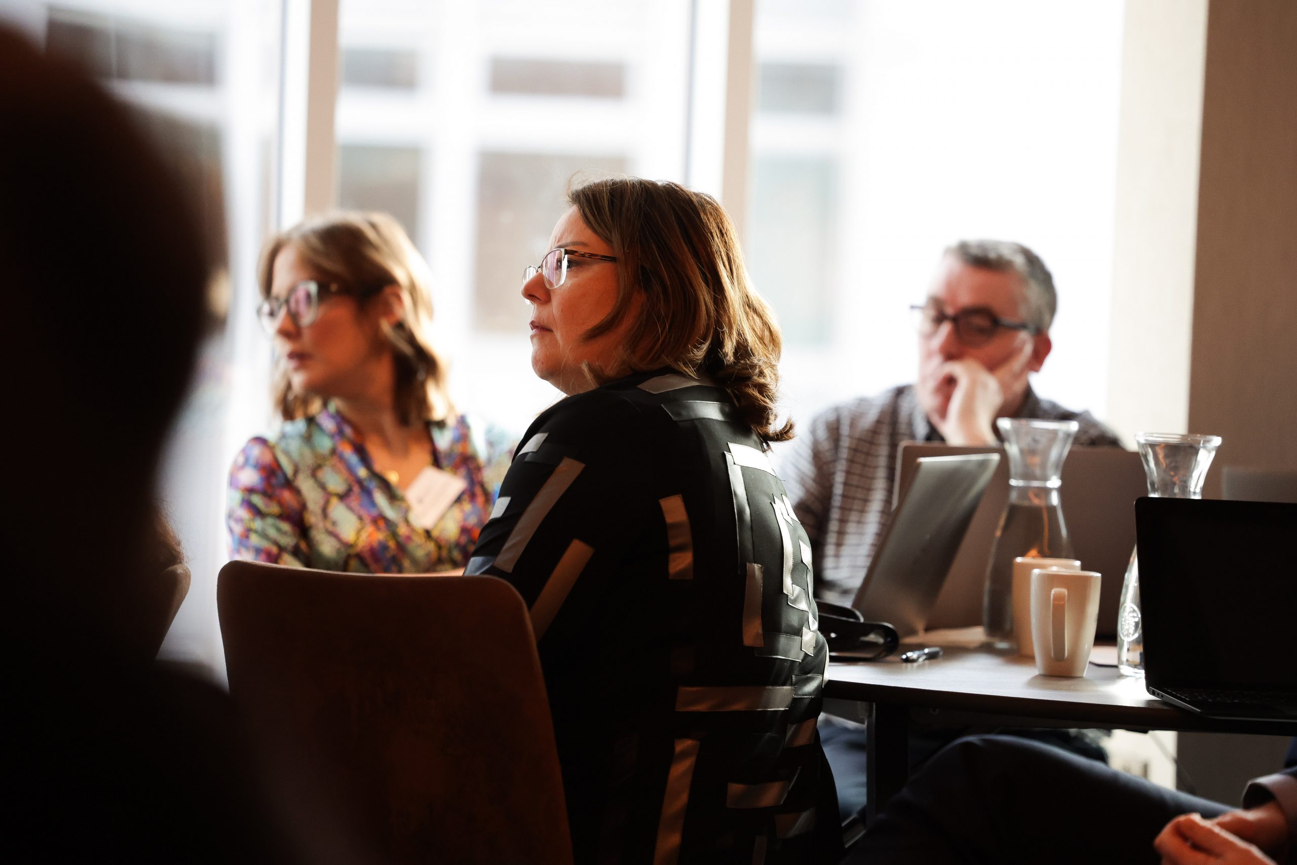 Attendees sit near large windows, listening to a discussion during a business or training session.