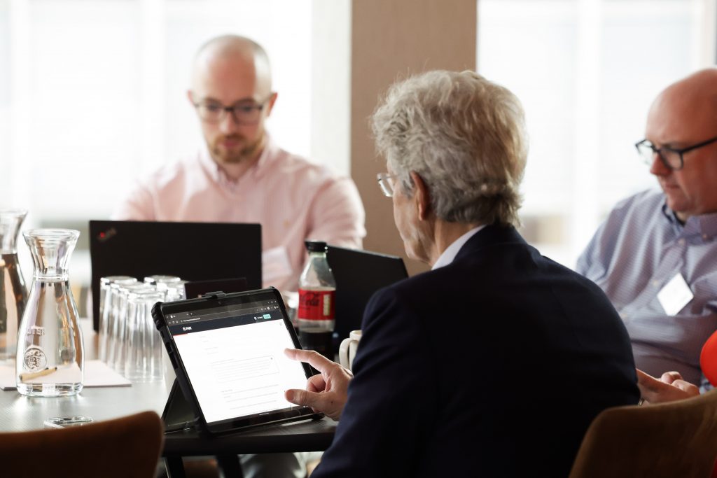 An Participant uses a tablet device while seated at a table with other attendees during an event.
