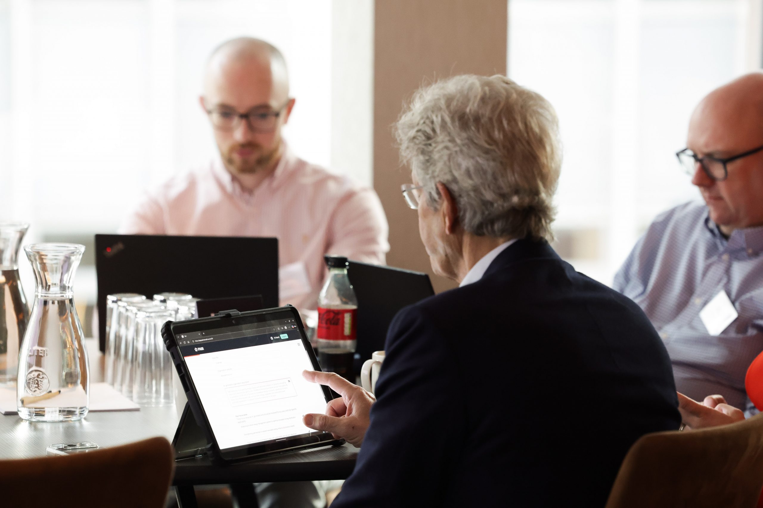 An Participant uses a tablet device while seated at a table with other attendees during an event.