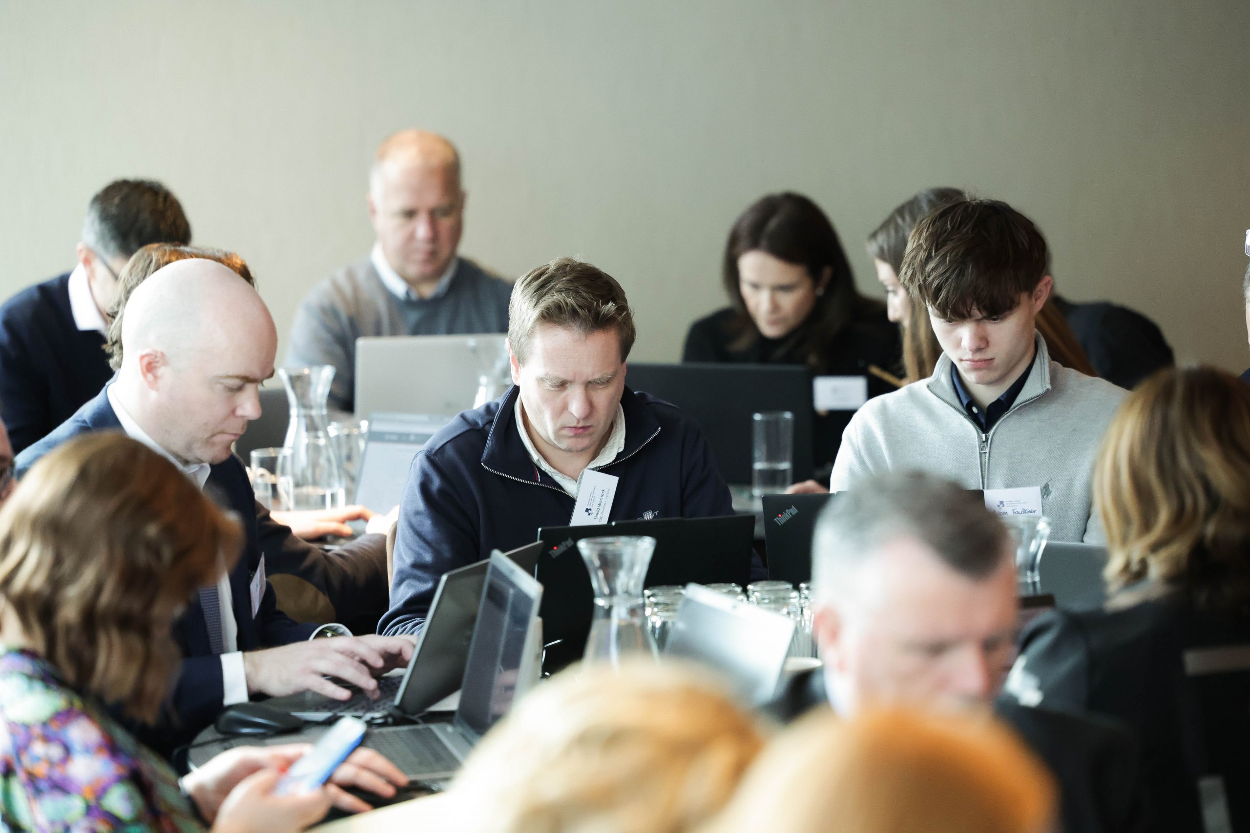 Participants seated at tables work on laptops and take notes in a collaborative learning environment.