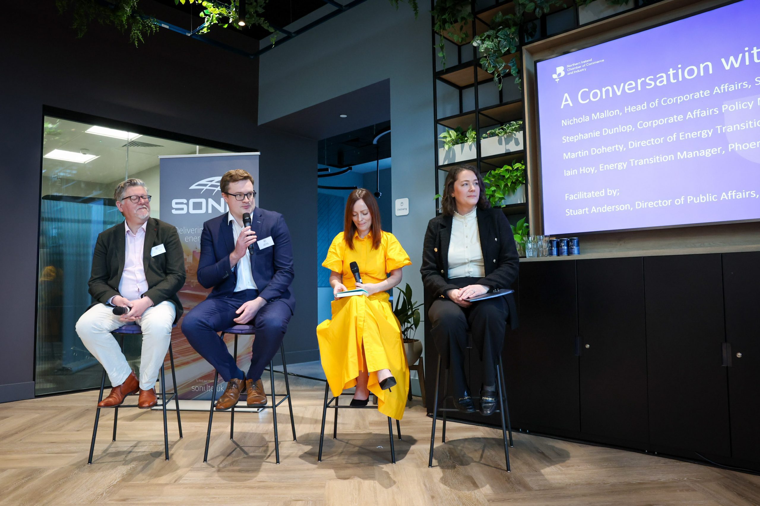 Four panelists sit on stools holding microphones during a discussion.