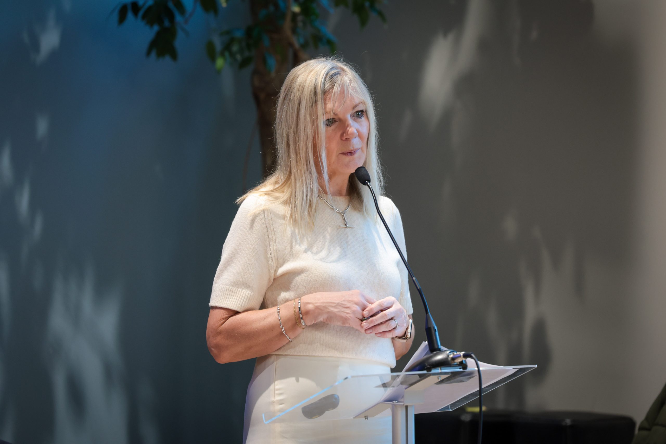 A speaker stands at a podium with notes, speaking into a microphone.