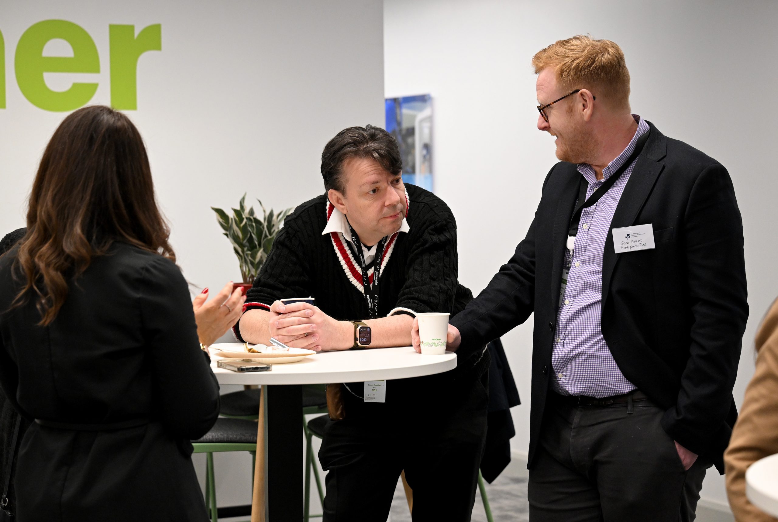 Three people stand at a tall table having a conversation during a networking session.