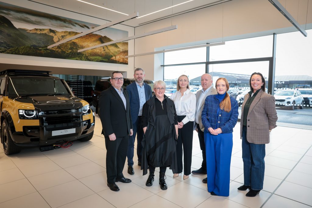 A group of event participants standing together for a group photo inside a showroom beside a vehicle.