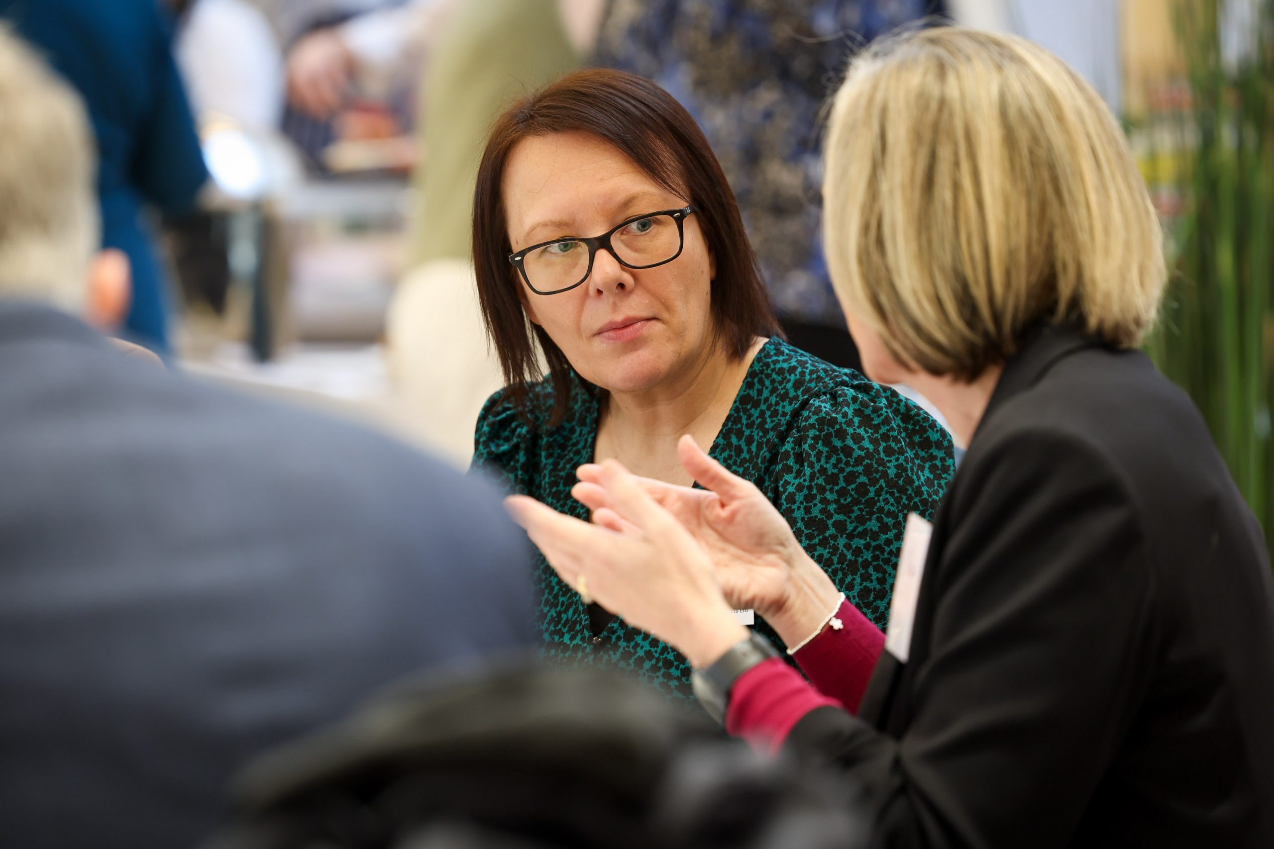 Two people engaged in conversation at a networking table, with one person gesturing with their hands.