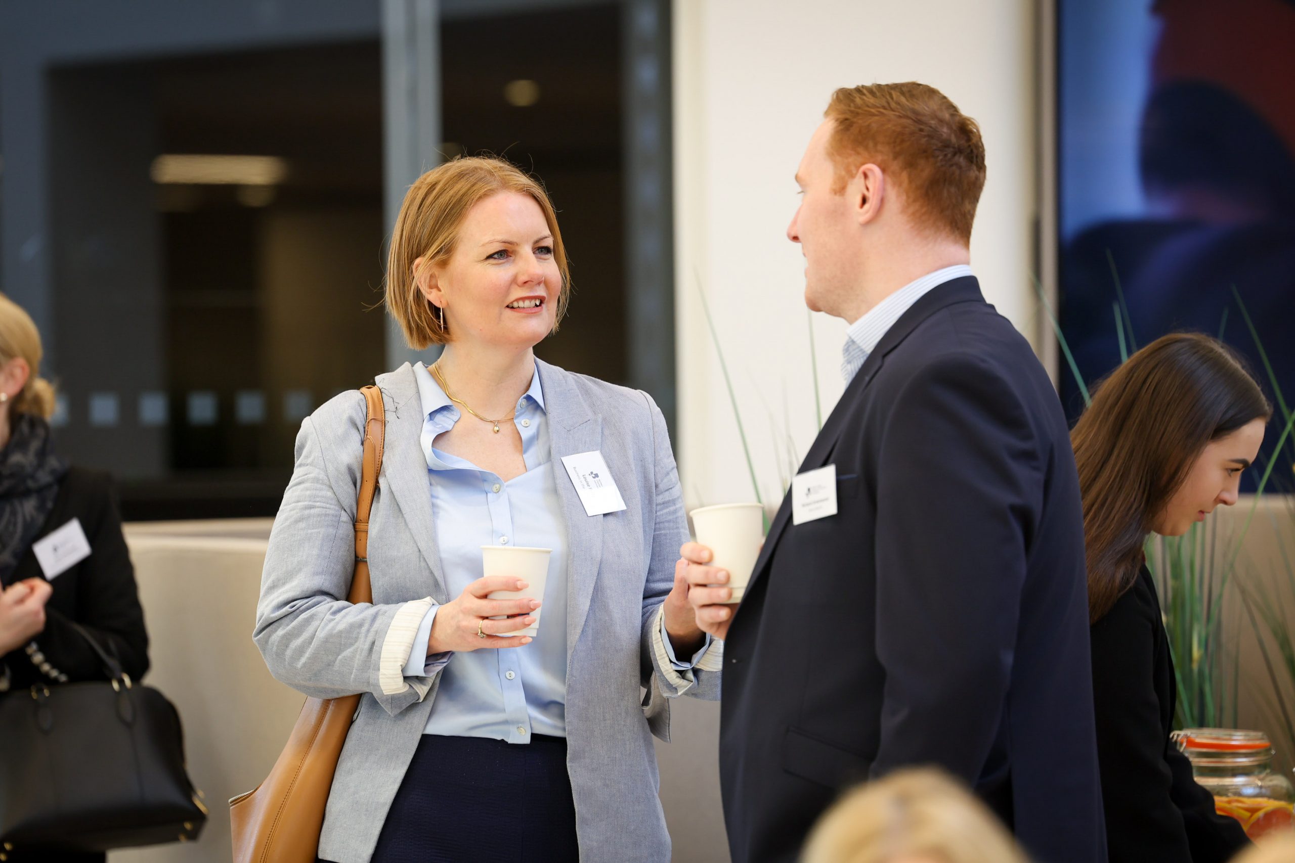Two people holding coffee cups while speaking during a networking break at a business event.