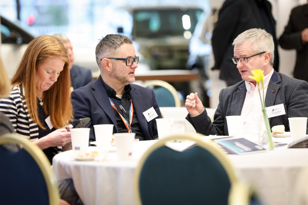 Three attendees seated at a table engaged in conversation during a business networking session.