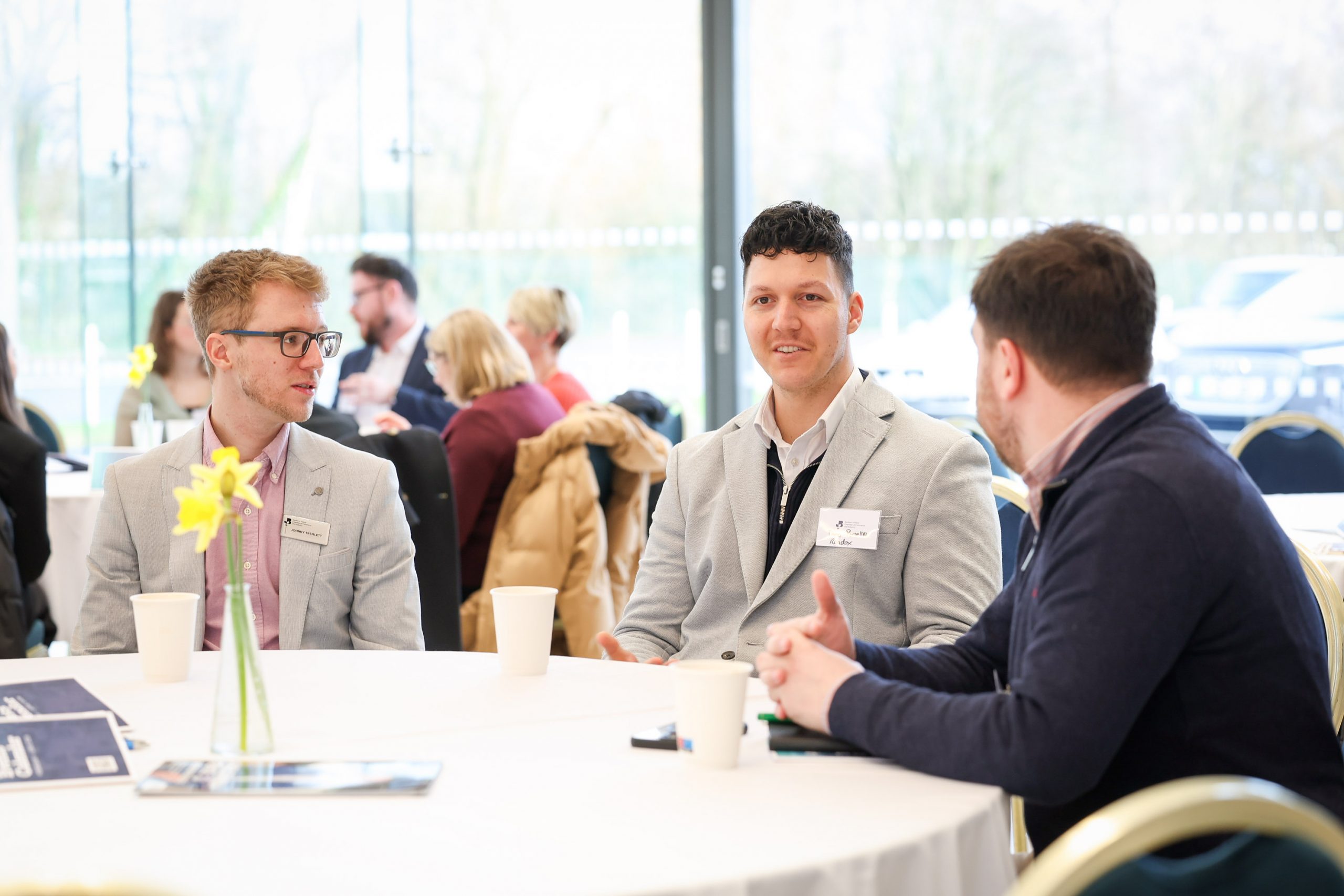 Three attendees seated at a round table talking during a networking session at an event.