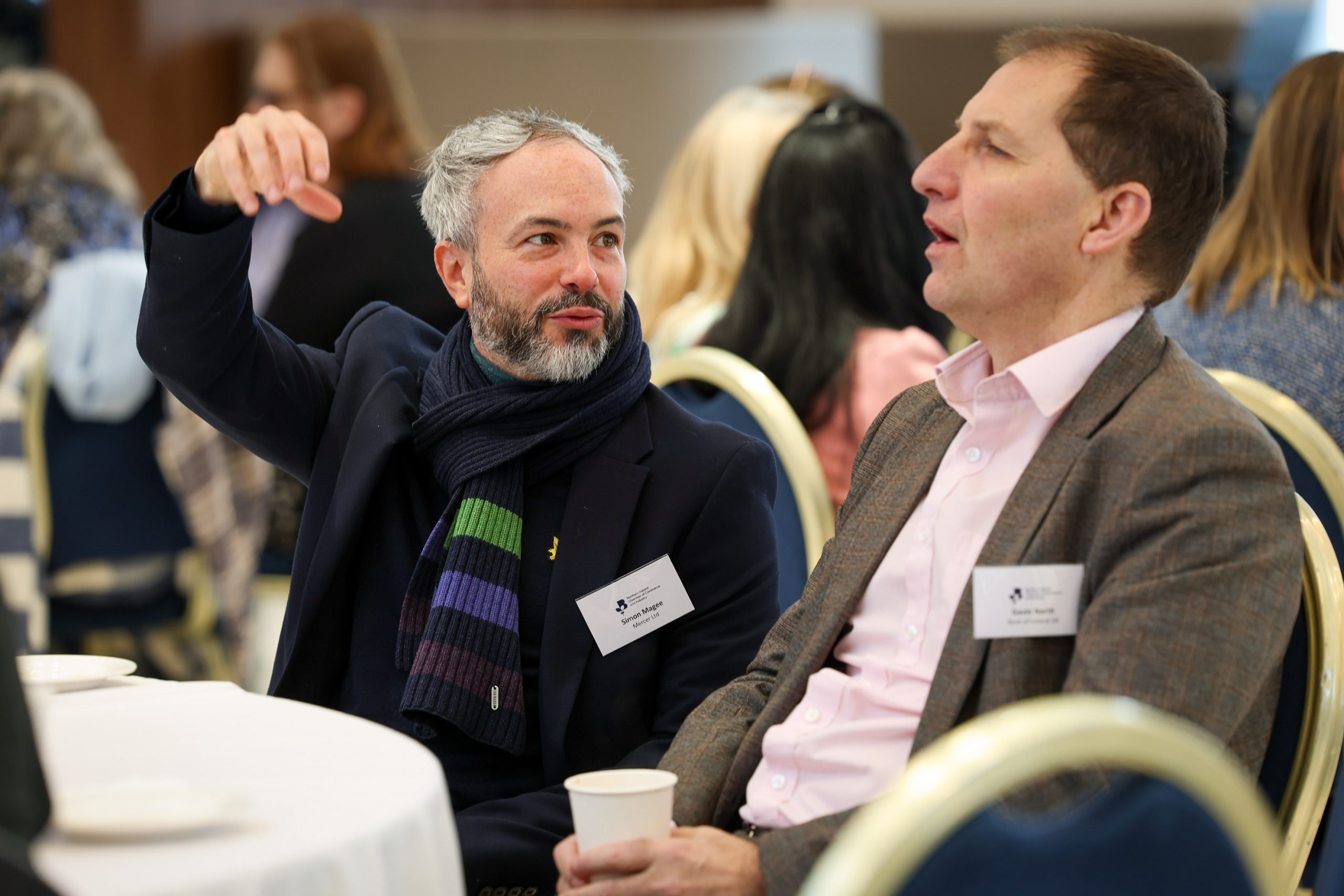 Two attendees seated at a table having a discussion, with one person gesturing while speaking.