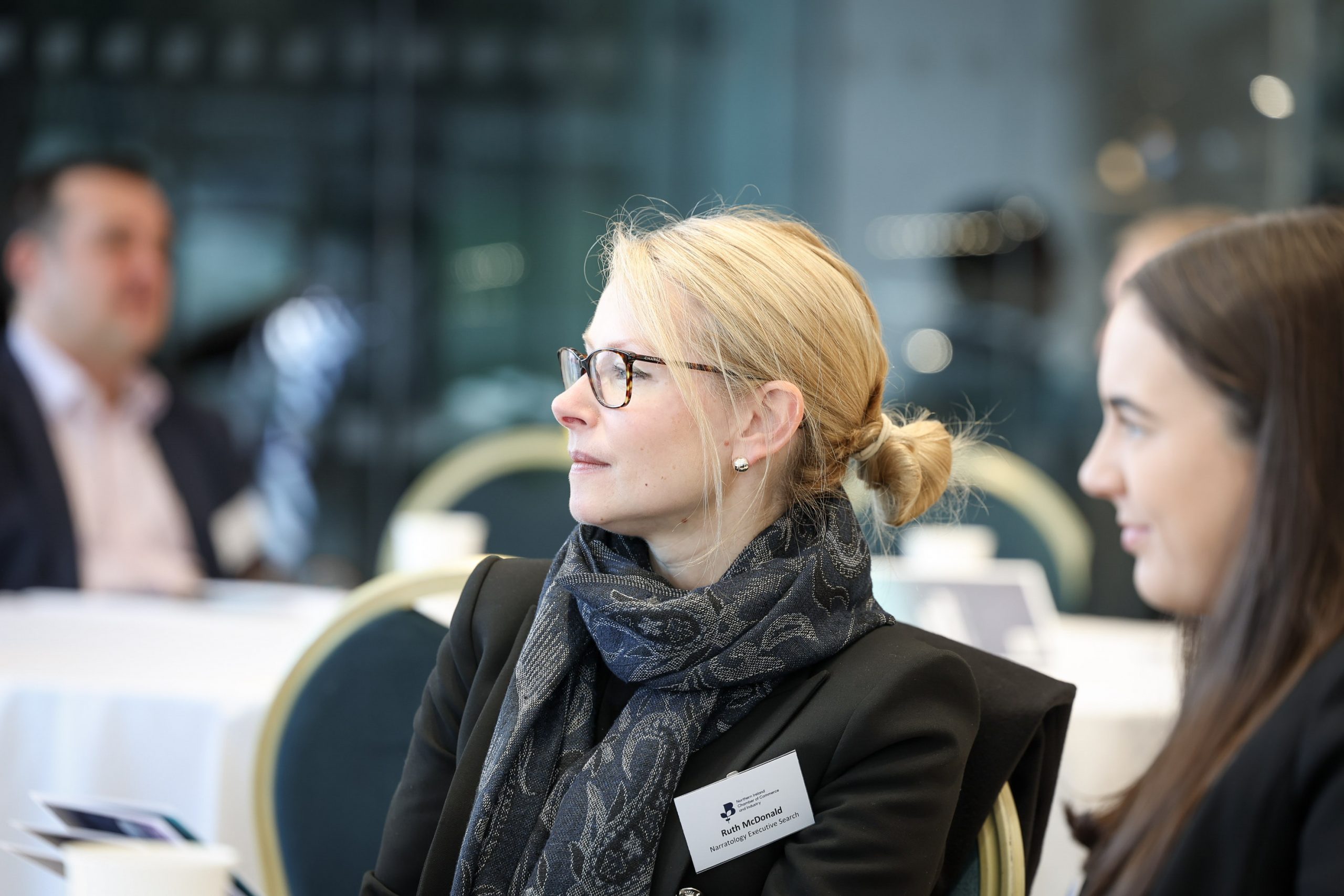 An attendee seated at a table looking toward the front of the room during a conference session
