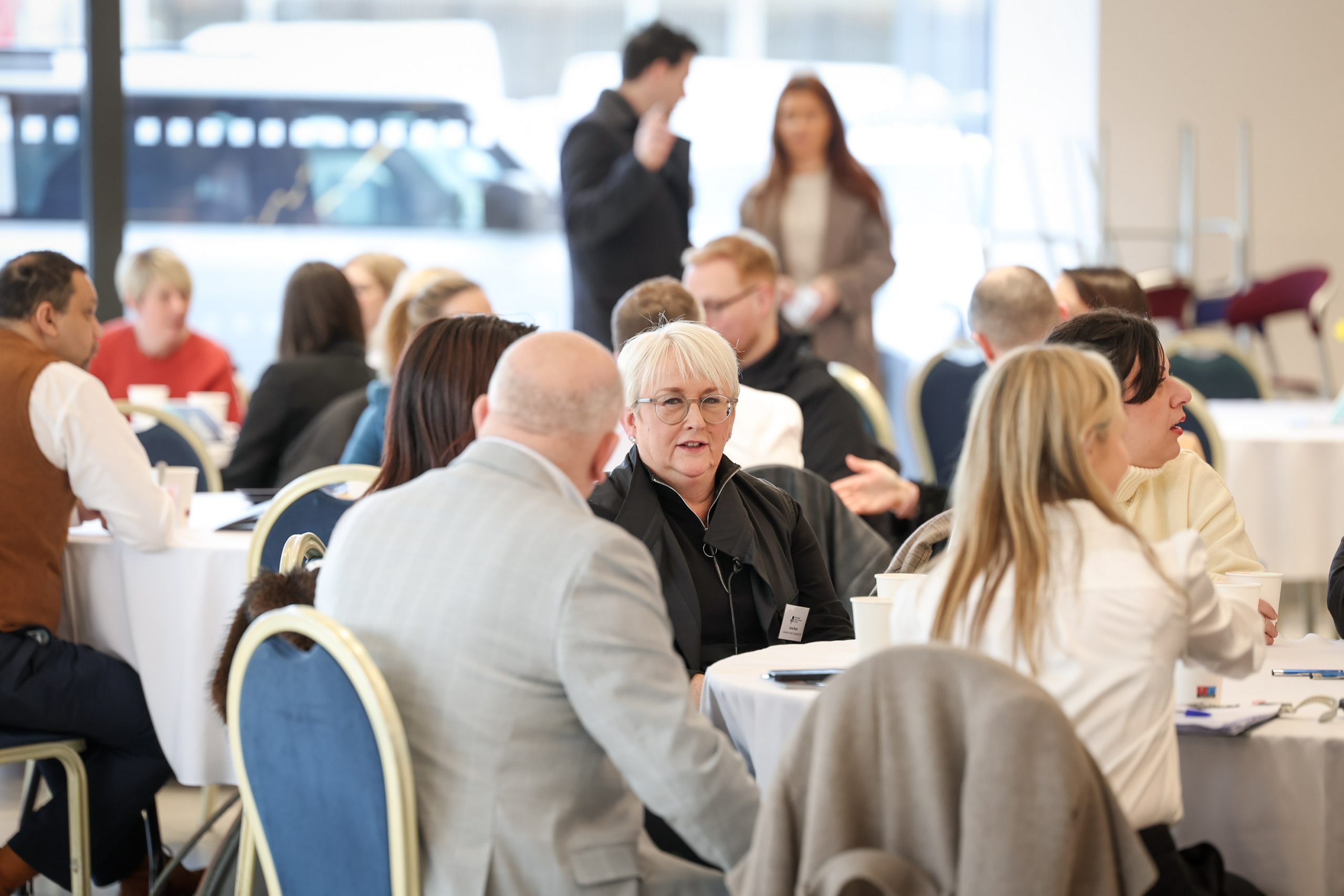 Groups of attendees seated at round tables, engaged in conversation during a business event.
