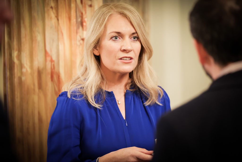 A person wearing a blue outfit engaging in conversation with others in a warmly lit room with decorated walls.