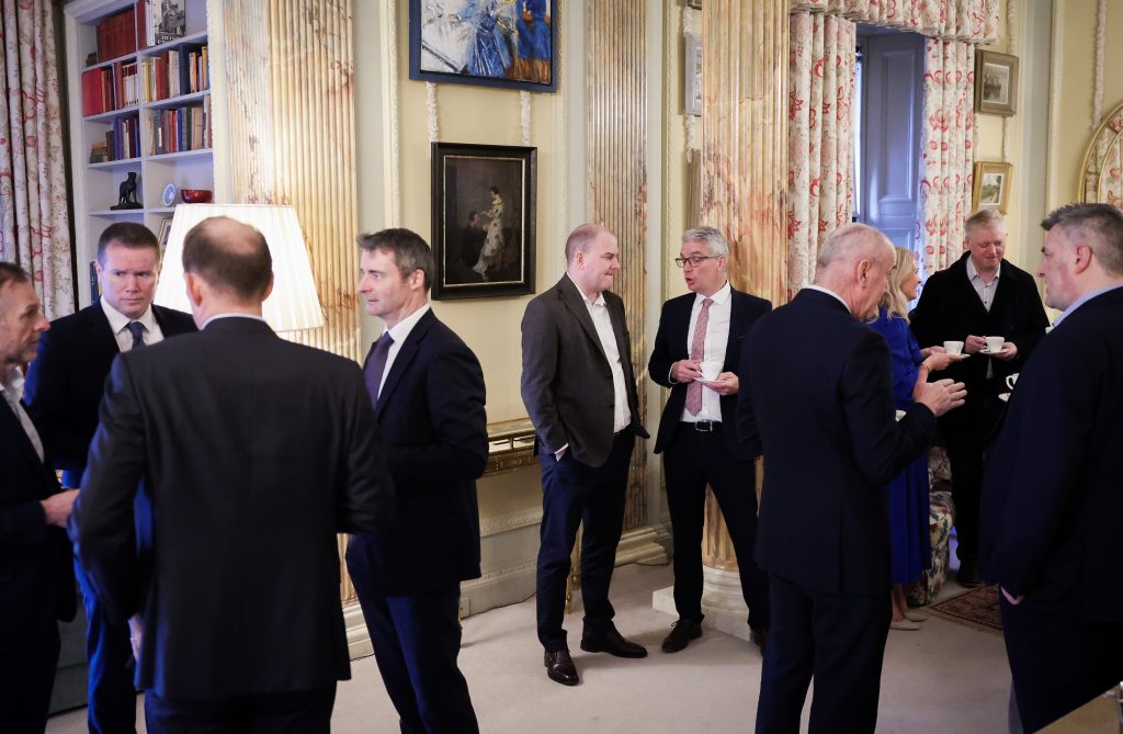 A wider shot of a group of people socialising in an ornate room, standing and talking in small groups.