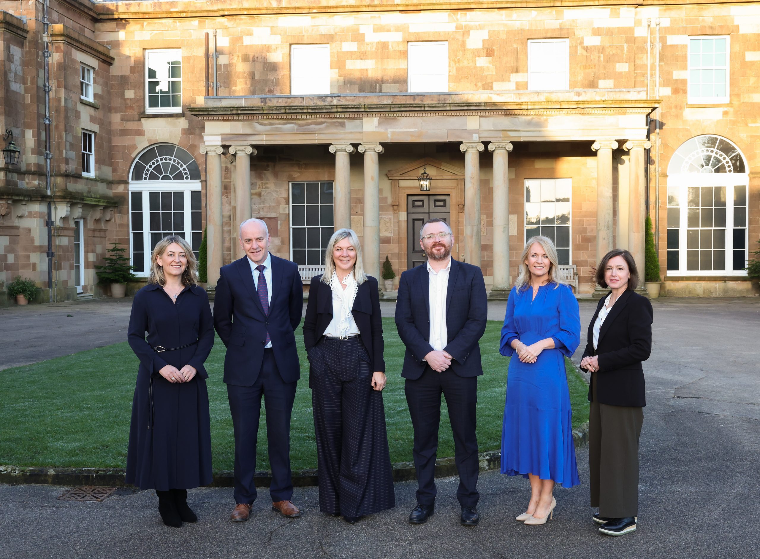 Six people standing outside a large historic building with columns, arranged for a group photograph.