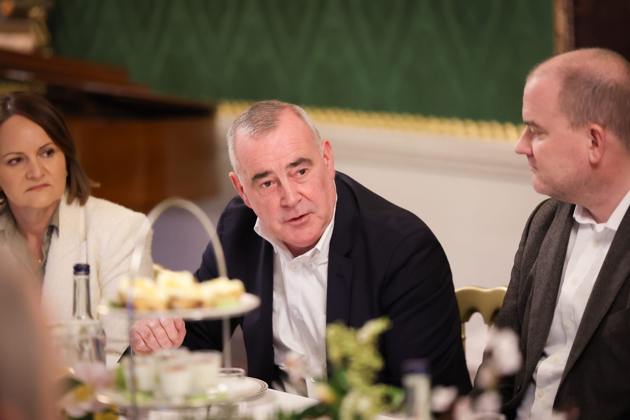 People seated at a table during a formal meal, with tiered trays of food and table decorations in the foreground.